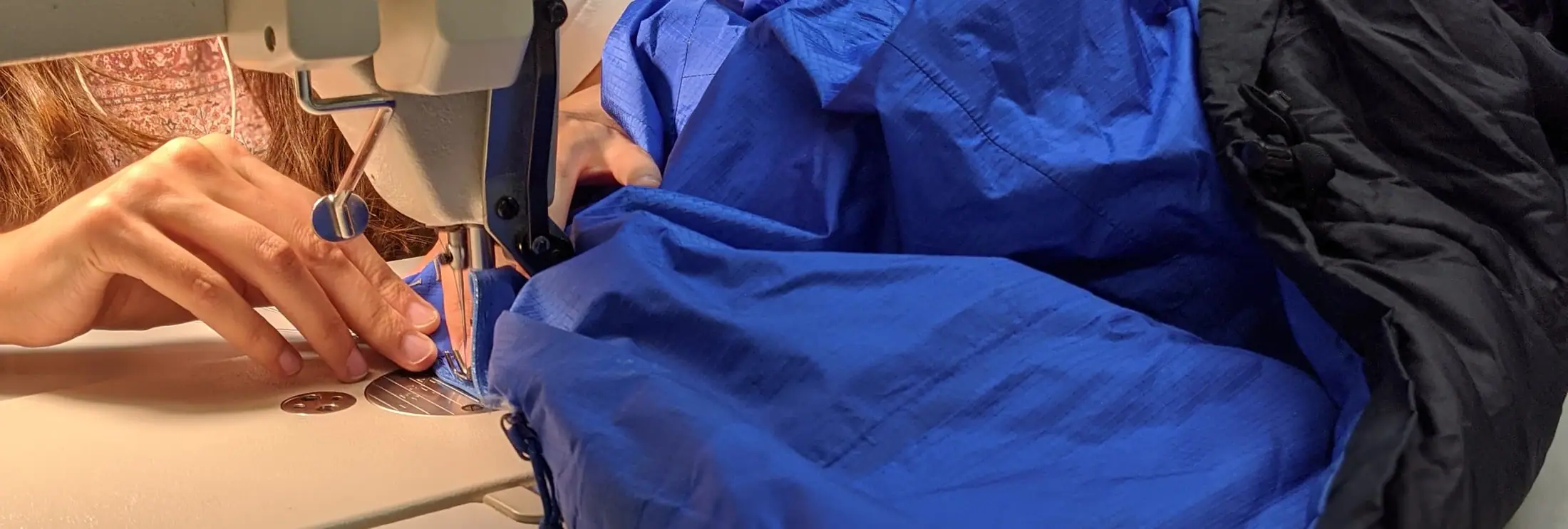 Technician sewing a blue waterproof jacket at Rainy Pass Repair
